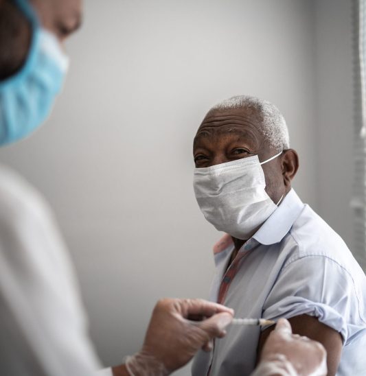 Nurse applying vaccine on patient's arm using face mask