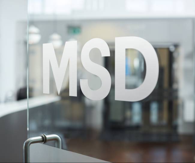 Logo MSD em adesivo em uma porta de vidro Em segundo plano temos um reflexo de um edifício