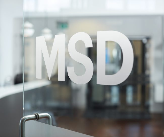 Logo MSD em adesivo em uma porta de vidro Em segundo plano temos um reflexo de um edifício
