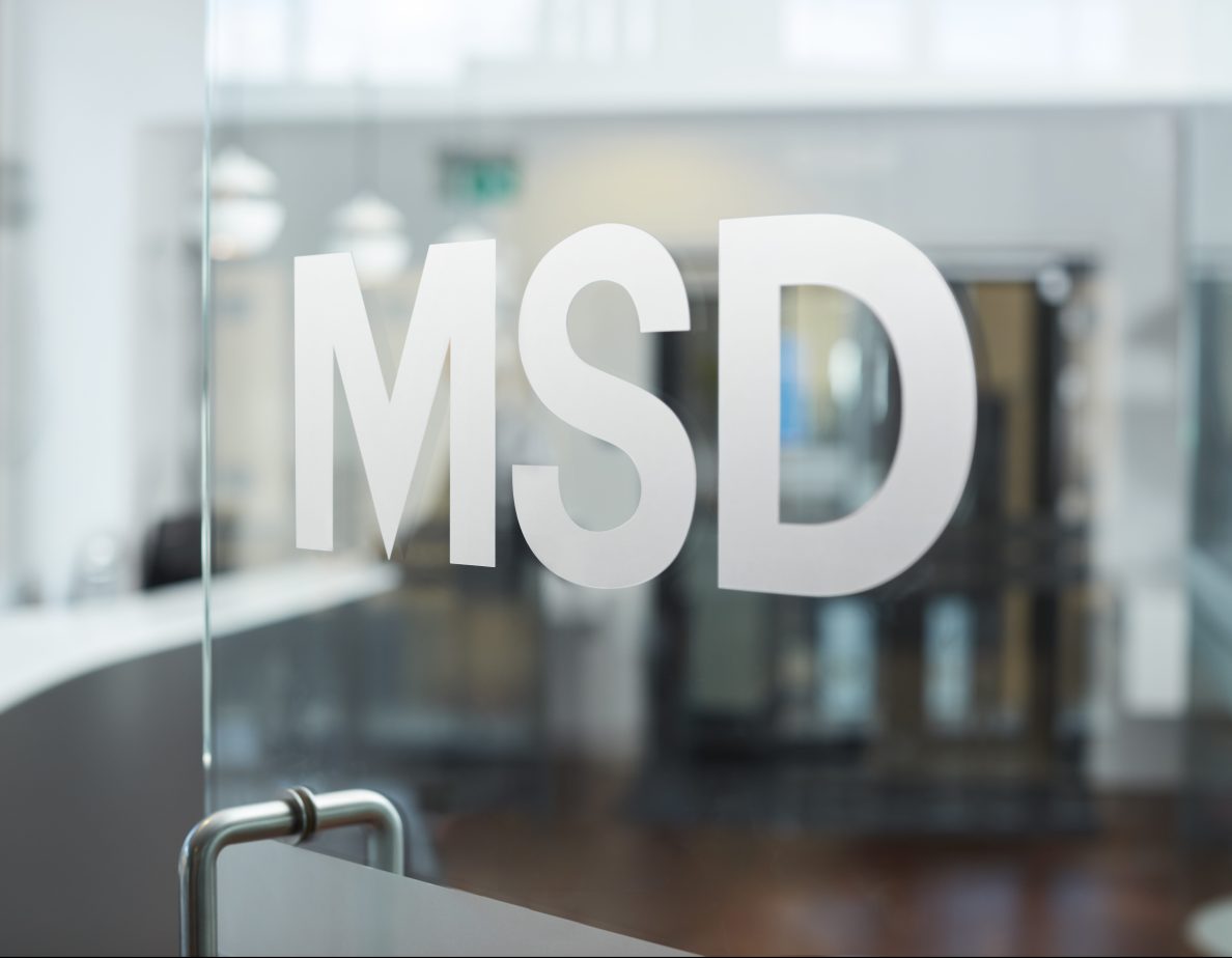 Logo MSD em adesivo em uma porta de vidro Em segundo plano temos um reflexo de um edifício